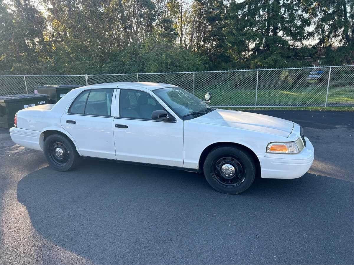 2010 Ford Crown Victoria for sale on Municibid, white in color, parked in a parking lot.