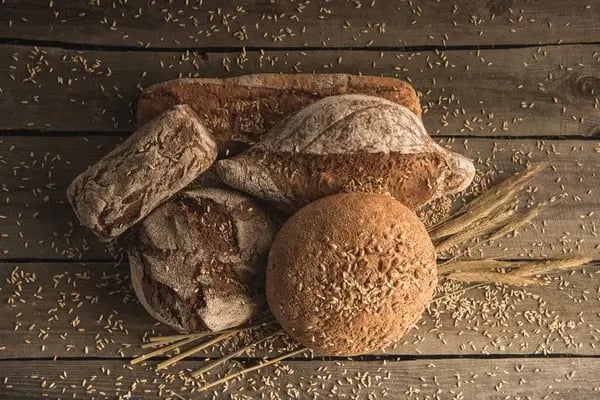 Whole wheat loaves on a rustic wooden surface with wheat scattered around them