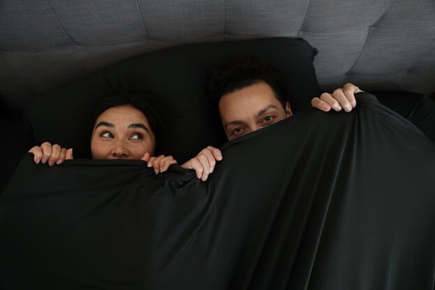 A Couple Hiding Under the Sheets in a Cold Room