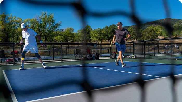 Pickleball players over 50 competing on an outdoor court despite knee pain