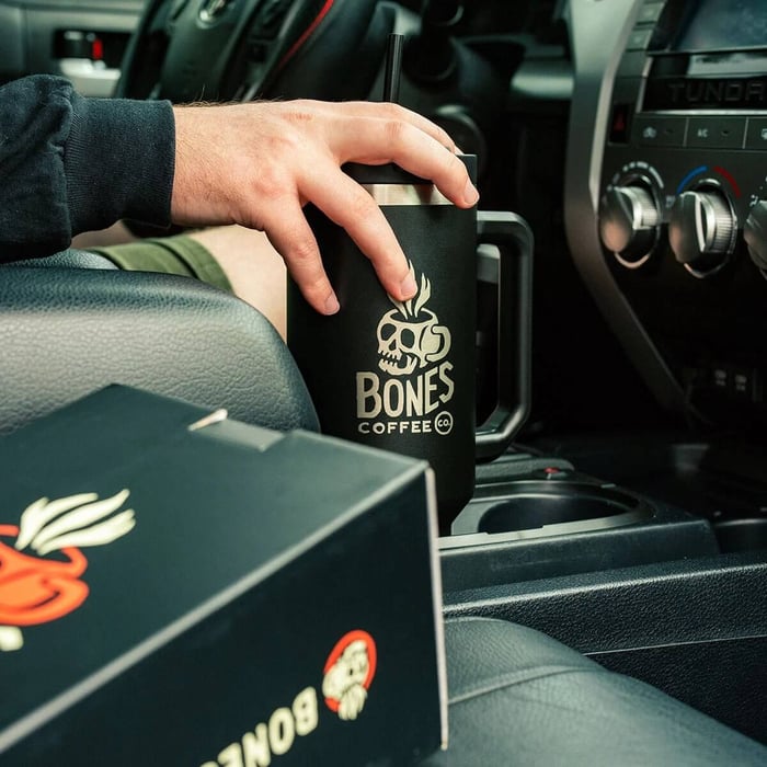 Hand holding Bones Coffee Company cup inside car.