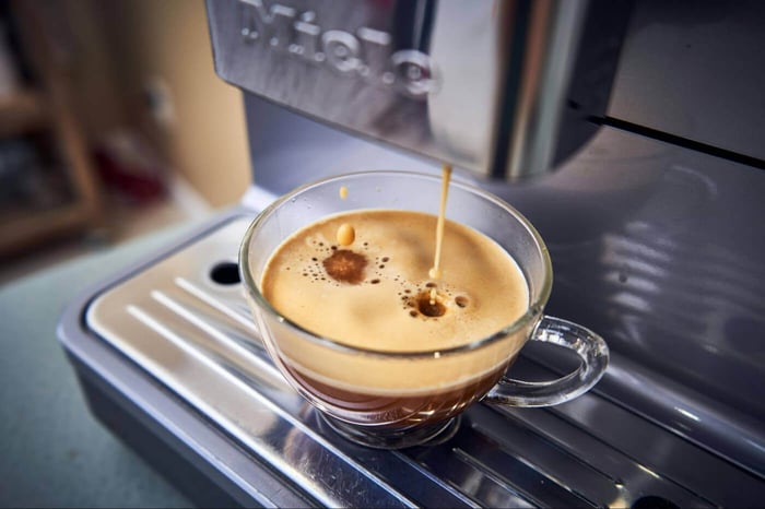 Fresh espresso pouring into a glass cup from an automatic coffee machine.