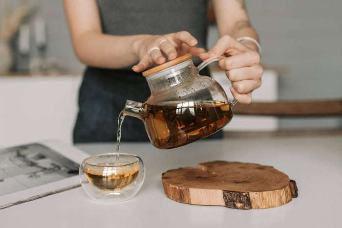 Woman pouring tea from glass teapot.