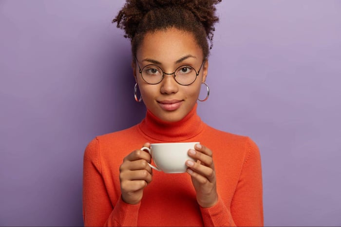 Person in glasses holding cup of coffee.