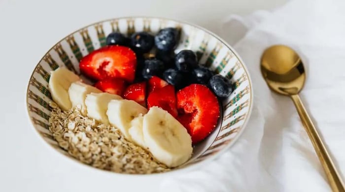 Blueberry overnight oats topped with fresh strawberries, banana slices, and blueberries served in a decorative bowl with a gold spoon.