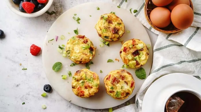 Egg breakfast cups with veggies served on a marble board alongside fresh berries, whole eggs, mint, and a cup of coffee for a complete morning spread