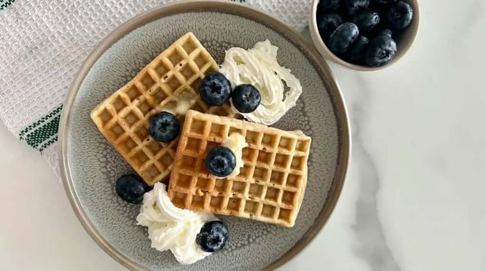 Healthy breakfast ideas featuring two golden waffles topped with fresh blueberries and whipped cream on a grey ceramic plate.