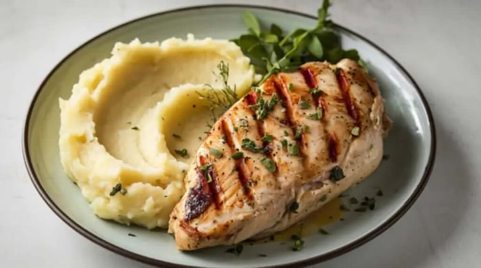 Healthy meal prep of herb-seasoned grilled chicken breast with creamy mashed potatoes and fresh greens on a sage green plate.