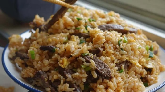 Healthy meal prep beef and vegetable stir-fry with red peppers and onions over steamed white rice in a ceramic bowl.
