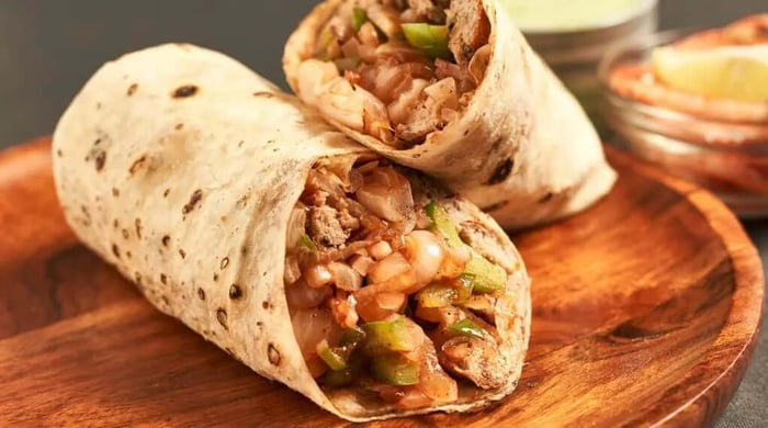 High protein burrito cut in half and filled with seasoned beef, beans, green peppers, and caramelized onions on a wooden serving board.