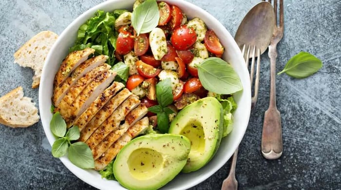 High protein chicken bowl with sliced grilled chicken breast, avocado, cherry tomatoes, fresh mozzarella, and basil pesto over mixed greens.
