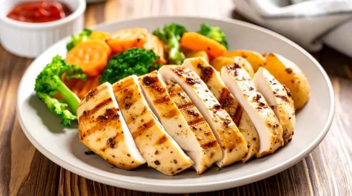 High protein food featuring sliced grilled chicken breast served with steamed broccoli, carrots, and roasted potatoes on a white plate.