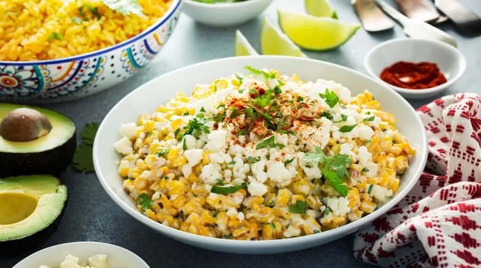 High protein meals with Mexican street corn salad topped with cotija cheese, cilantro, and chili powder served alongside avocado and yellow rice.