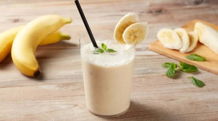 Peanut butter banana protein shake in a glass garnished with banana slices and fresh mint on a wooden surface.