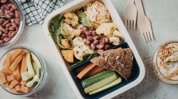 Plant-based lunch box with roasted cauliflower, kidney beans, arugula, hummus, cucumber, carrot sticks, and seeded crispbread for healthy meal delivery.