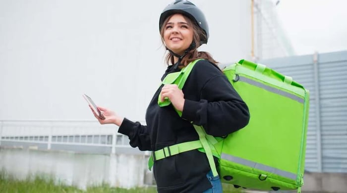 Prepared meal delivery for weight loss with a delivery courier wearing a helmet and green insulated backpack holding a smartphone.