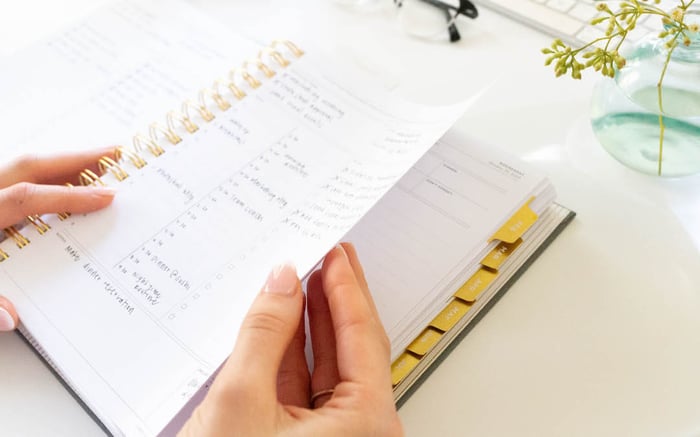 tackling overwhelm with day designer planner, open book with written on page, hands, vase with flowers