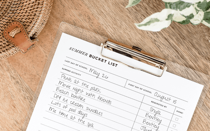 day designer summer bucket list printable with writing to show examples of use, attached to clipboard, flowers, wicker basket