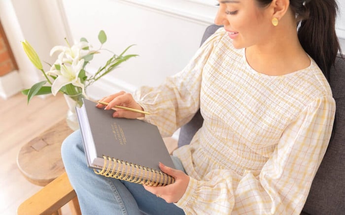 woman holding gray day designer planner with gold binding, practicing positivity