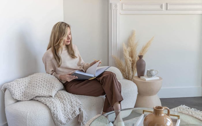 kick off your day with a plan, woman sitting on white couch holding open planner, blanket, coffee table, vases, dried wheat