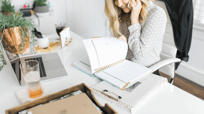 organize your life, woman sitting at desk with open planner, laptop, glass of water, plant, stationery