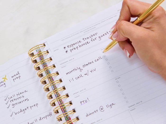 plan your ideal week, day designer open book weekly planner with written on pages, light green background, pens, paper clips, eye glasses