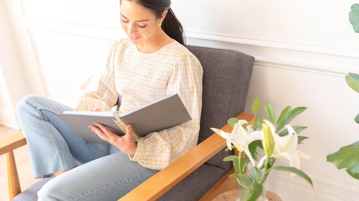 woman sitting in chair with open planner, flowers in vase, planning gives your life direction