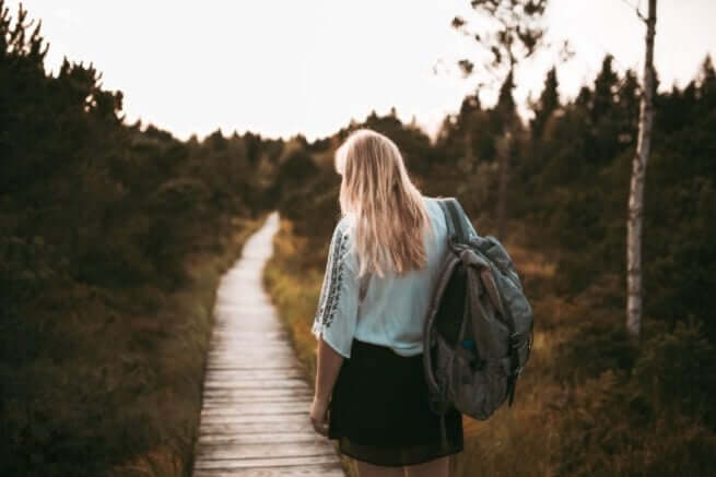 woman implementing a self care plan, wearing a backpack, walking on path, trees