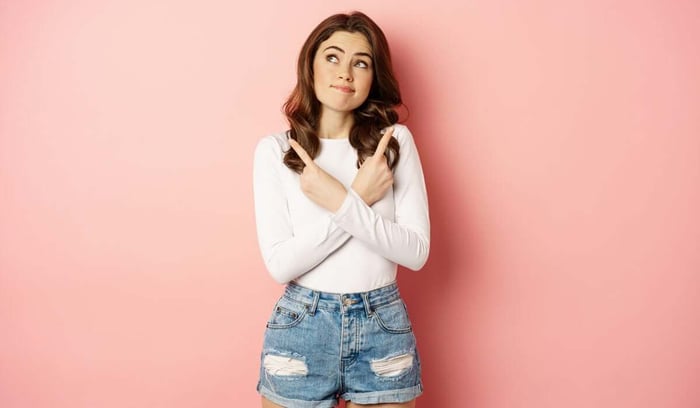 Contemplating woman pointing in two directions against pink background