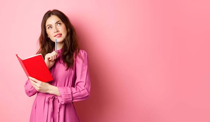 Thinking woman holding red notebook against pink background