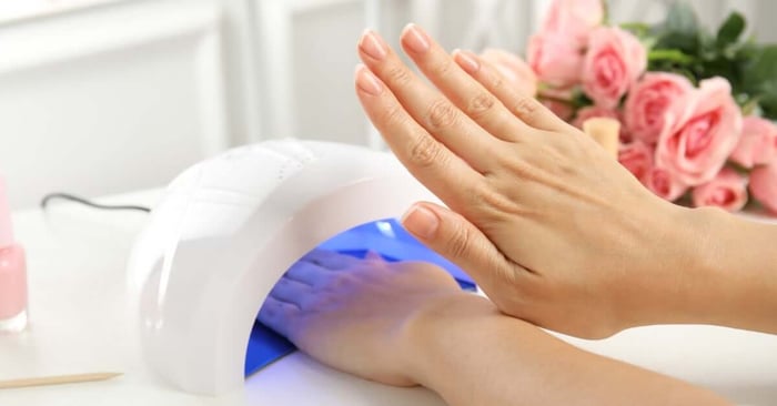 A woman is observing the nails on one of her hands while the other hand is under an ultraviolet lamp.