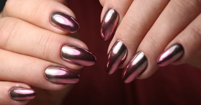 A close-up of a trendy metallic purple and green design of acrylic manicure on long, almond-shaped, rounded nails.