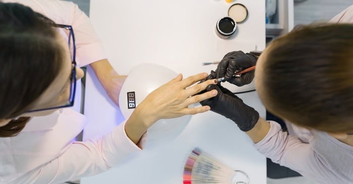 A manicurist is doing a manicure for a client and using an ultraviolet lamp for fixing gel nail polish.