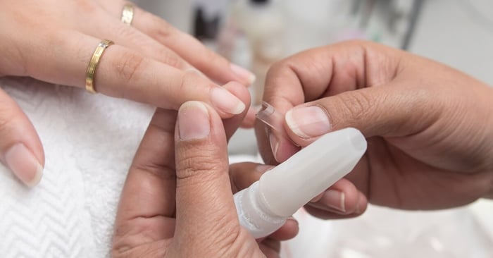 A technician holding a client's finger still while visually measuring and matching an acrylic extension against their nail.