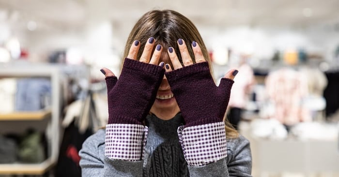A person in a department store lifting their hands over their face. They have fingerless gloves on and painted nails.