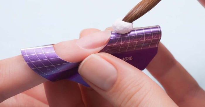 A nail technician placing a bead of acrylic onto a nail form to achieve a longer nail for their manicure client.