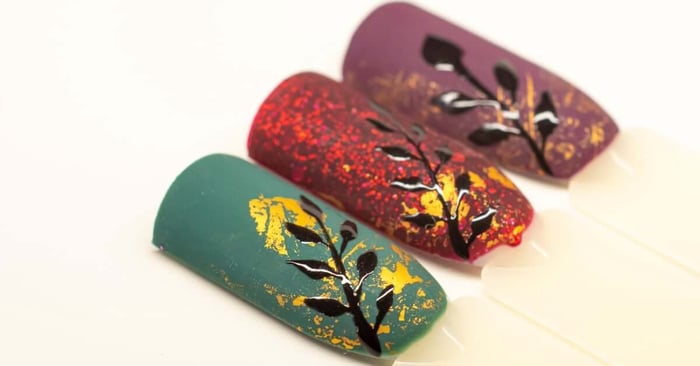 A set of three example nails in jewel tones, including green, red, and purple, with gold foil accents on each.