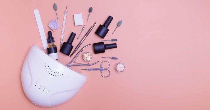 A close-up of a manicure lamp, tools, and bottles for applying varnish. They're all scattered across the table.