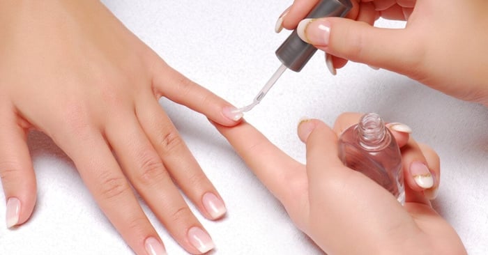 A close-up of someone getting their nails done by a professional nail tech. The nail tech is applying clear nail polish.