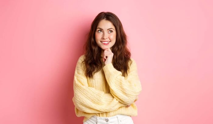 Smiling woman in yellow sweater thinking against pink background
