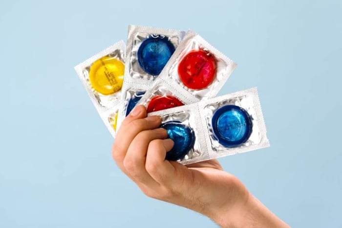 Multiple condoms in different colors held by one hand.