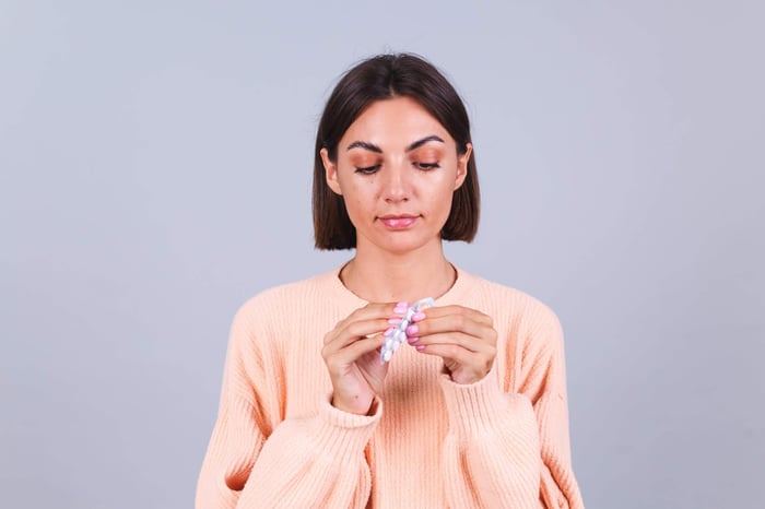 Woman holding birth control pill pack against gray background.