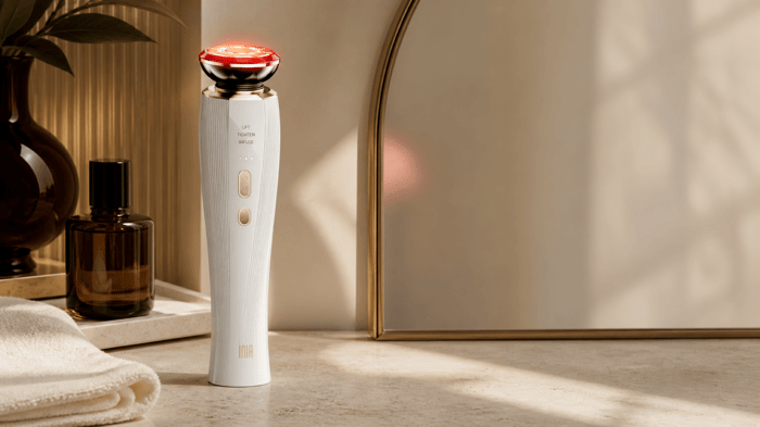 INIA FLARE Microcurrent Facial Device on a bathroom vanity beside a folded towel and mirror