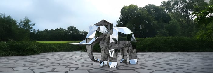 Reflective geometric elephant sculpture on a stone patio surrounded by lush greenery.