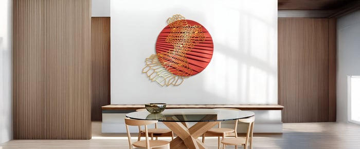 Modern dining room with round abstract red and gold 3D wall sculpture and glass-top wooden table.