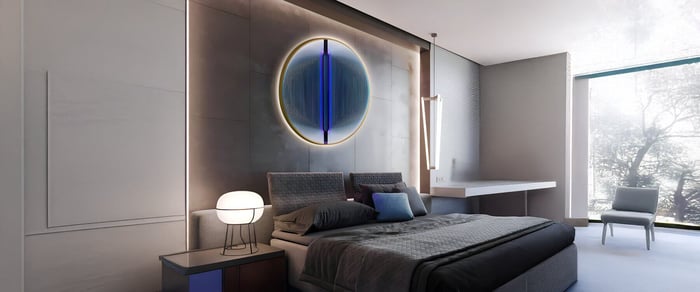 Circular LED bedroom art with blue accents above a modern bed in a softly lit minimalist bedroom.
