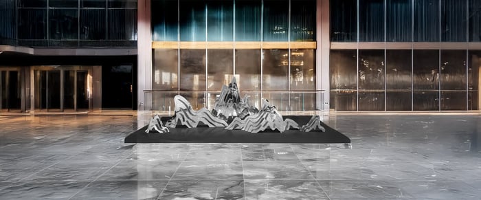 A contemporary, large-scale metallic mountain-inspired sculpture placed in a modern lobby space with marble flooring.