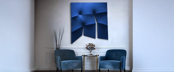 Contemporary nook with deep blue abstract 3D wall art above a pair of matching velvet chairs and a round metallic table.