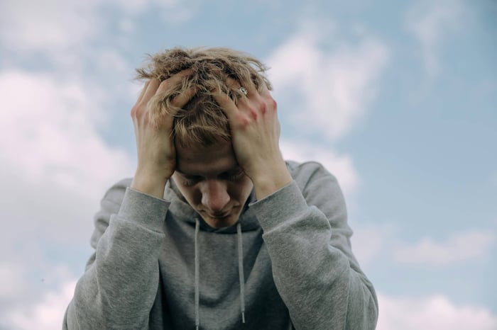 A young man sits outside with his head in his hands.  His body language communicates that he is not feeling well, the absence of creatine in the image suggests something is missing in this person's life.