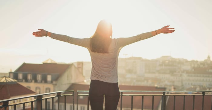 A person on a balcony with arms spread embracing the morning light as part of a series of morning habits to implement in the morning